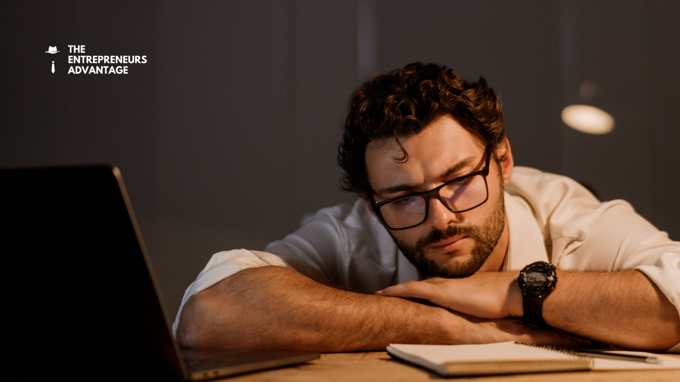 The Invisible Profit Killer_ How _SaaS Bloat_ is Quietly Stalling Your Business Growth A stressed entrepreneur resting his head on his desk while working late at night on a laptop, representing the exhaustion caused by SaaS bloat and managing too many software tools.